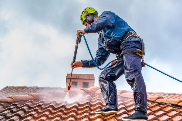 A worker pressure washes a roof